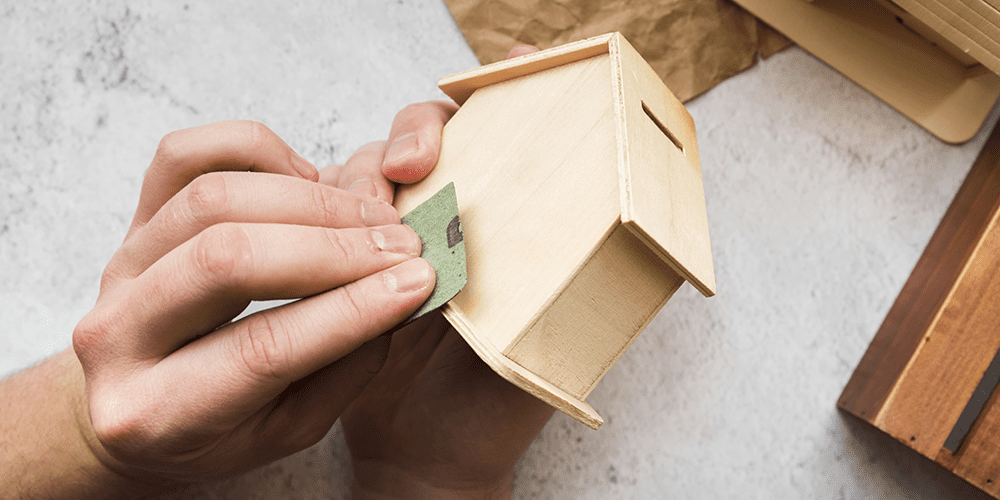 woman-s-hand-smoothing-wooden-piggybank-house